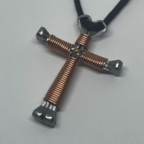 A small copper cross of nails necklace on a black cord. 