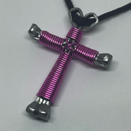A small pink cross of nails necklace on a black cord.
