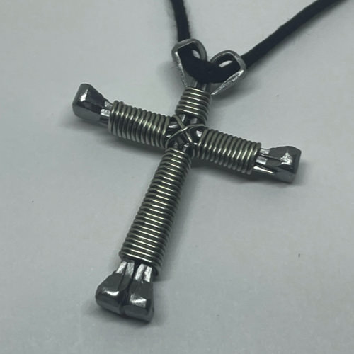 A small silver cross of nails necklace on a black cord.